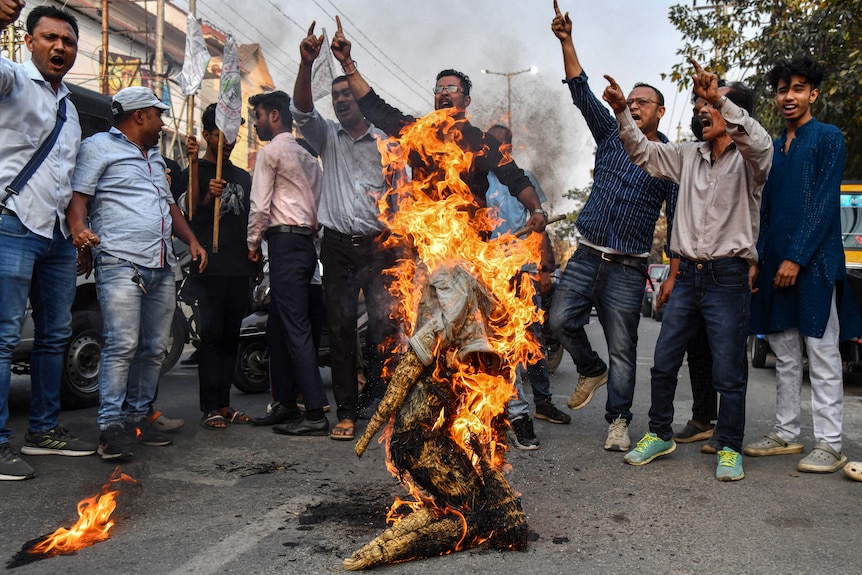 An effigy of India's president is burned with people chanting around.