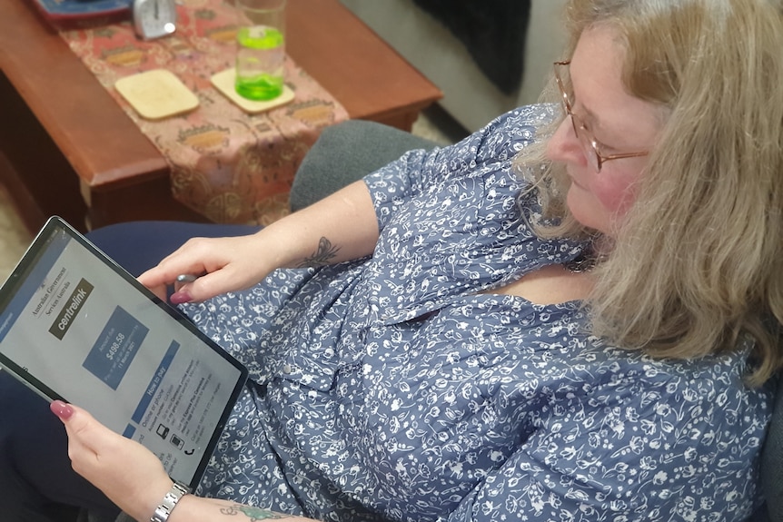 a woman sitting on a chair looking at a centrelink website on her ipad