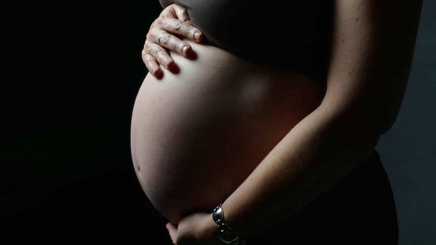 A pregnant woman holds her stomach, only hands and stomach are pictured