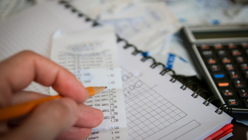 Close up shot of a hand holding a pencil above a receipt, with notebook and calculator also in shot