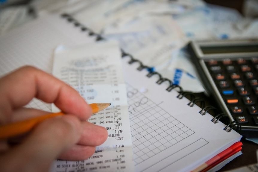 Close up shot of a hand holding a pencil above a receipt, with notebook and calculator also in shot