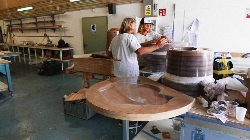 Andrew Turton and Pete Ceglinski stand in a workshop looking at a prototype Seabin.