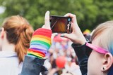 A young woman at an LGBT pride festival takes a photo.