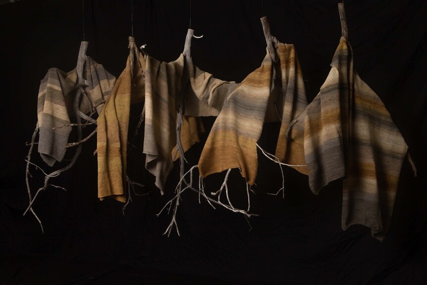 Multi-coloured  fabric in muted greys and yellows, hang on wires on branches.