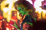 A drag queen holding a drink, in profile against a neon background.