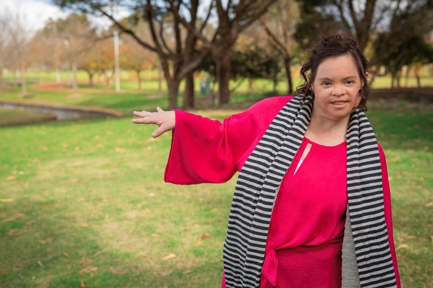 A woman gesturing with one arm in a grassed setting.