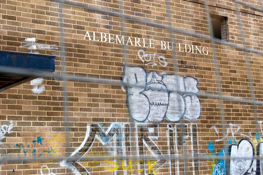 A sign reading Albemarle Building, with a missing 'i' on a building covered with graffiti.