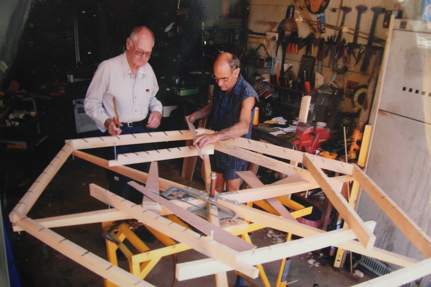 An older photo of two men working on rebuilding a timber windmill frame.