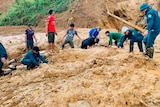 Villagers and soldiers use their hands to search through thick mud brough down in a mudslide