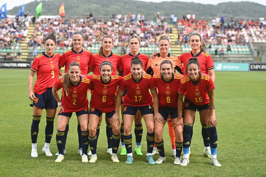 A women's soccer team wearing red, blue and yellow poses for a photo