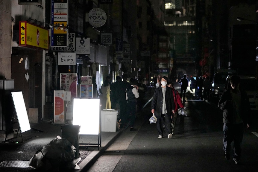 People walk along a busy street in Japan in darkness.