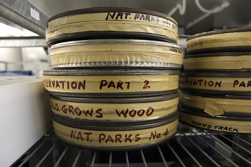 A stack of labelled film reels in metal tins sitting on a shelf in a cold room.