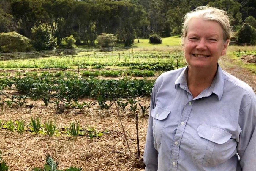 A woman smiles at the camera with rows of vegetables behind her.