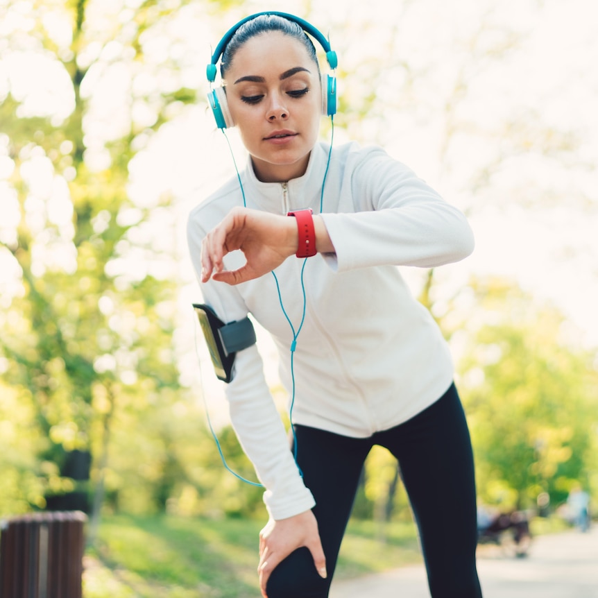 Young woman exercising in the park and checking data on smartwatch