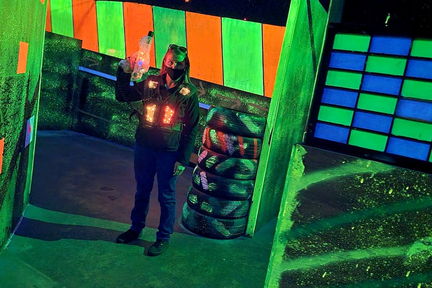 A woman in a vest holding a laser tag gun surrounded by tyres and spray painted walls.