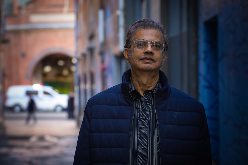 A man stands in an alley, looking into the camera.