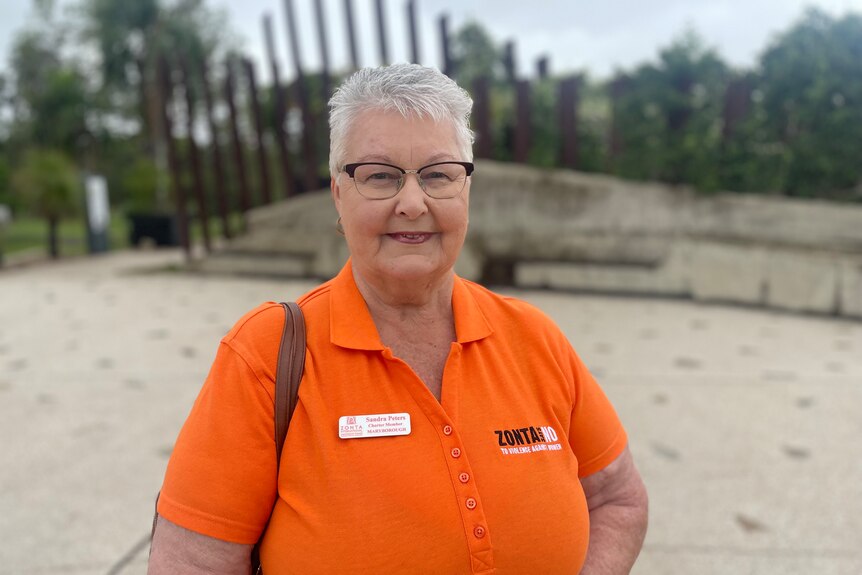 A woman in a bright orange shirt and glasses smiles 