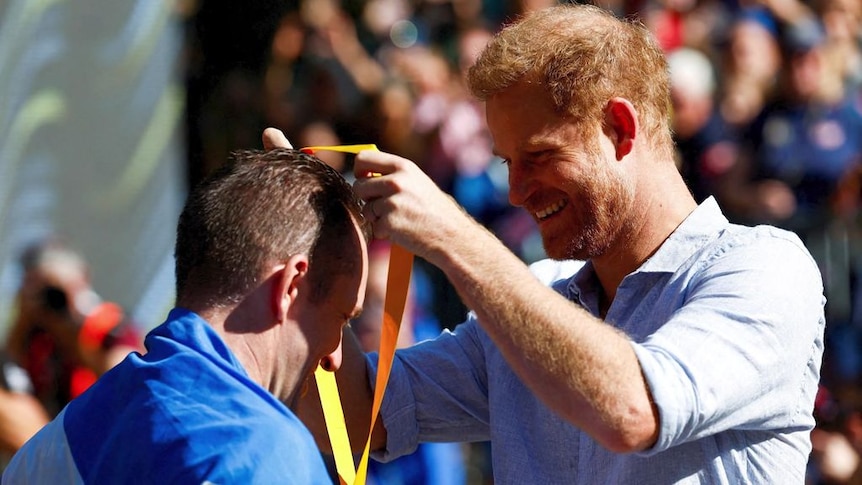 Prince Harry places a medal around the next of a man draped in a flag.