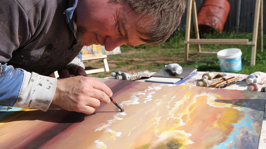 An artist smiles as he paints in his open air studio