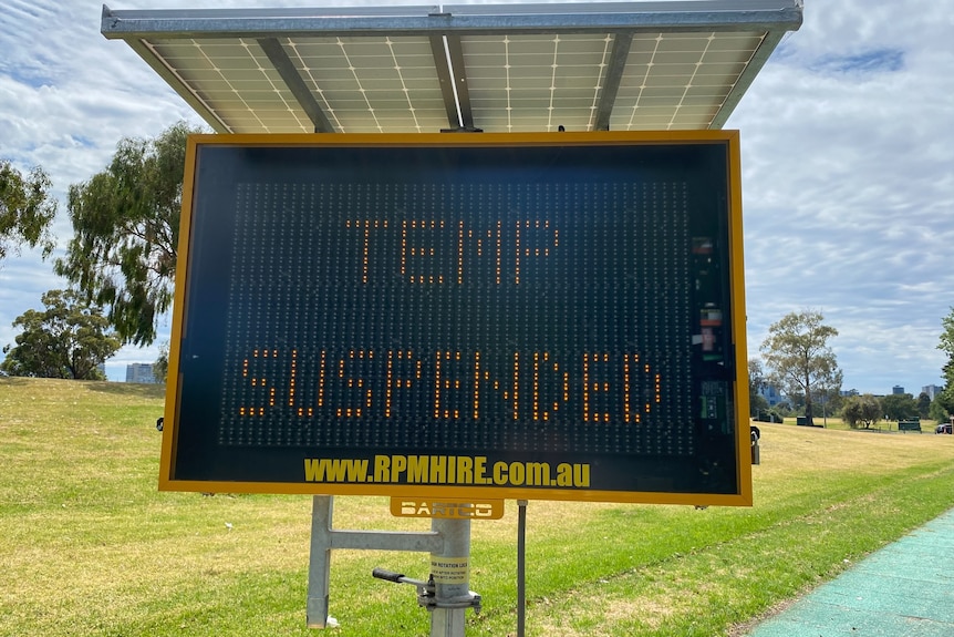 Digital road sign displaying "Temp Suspended' in front of green field.