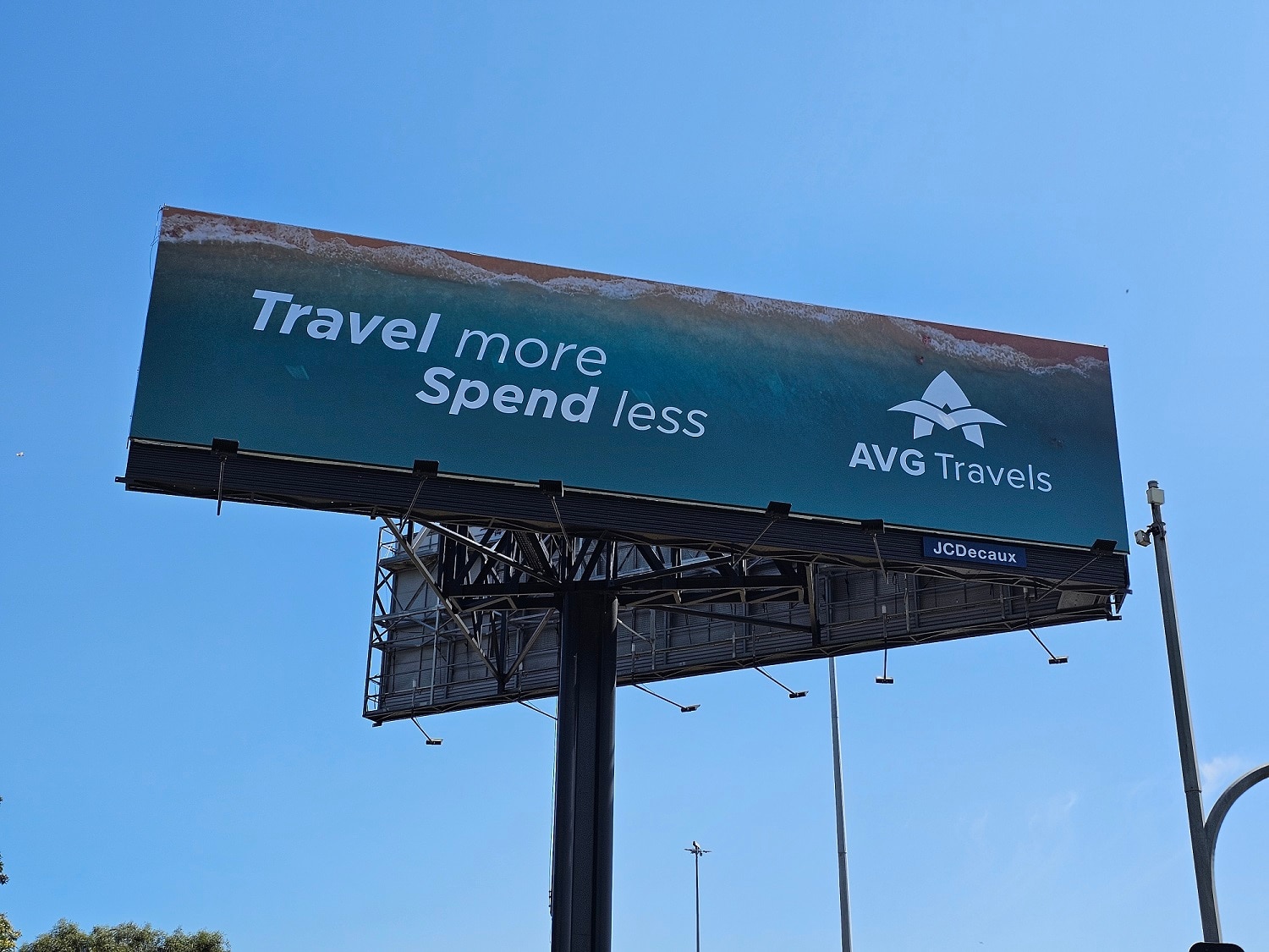 A large advertising sign saying "Travel more, spend less" and the AVG Travel logo.