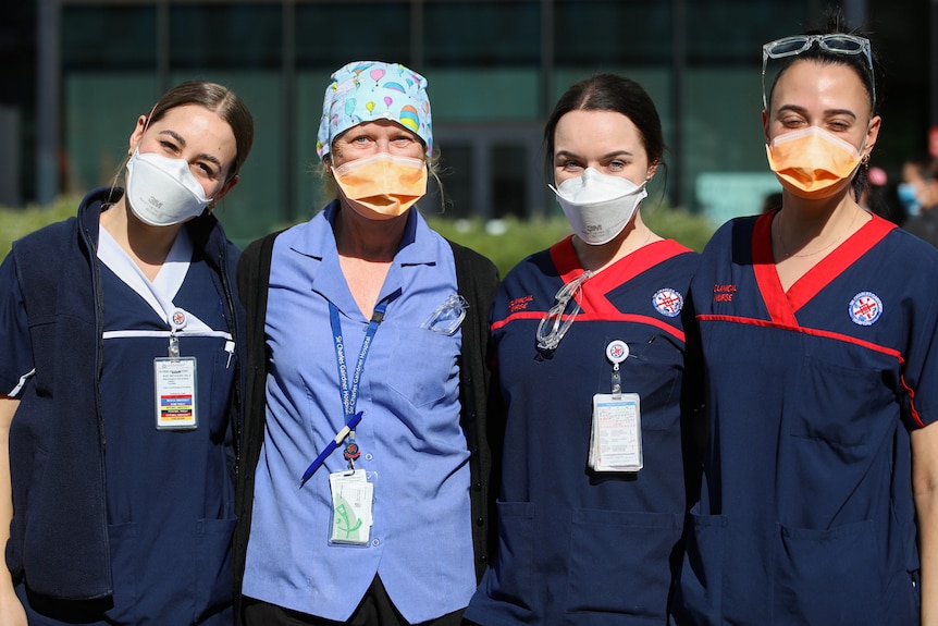 A group of four health staff in uniform and masks stand next to each other.