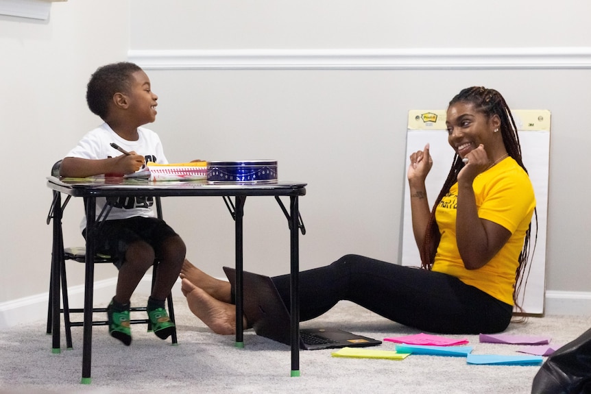Woman with small child at desk smiling as they do school work