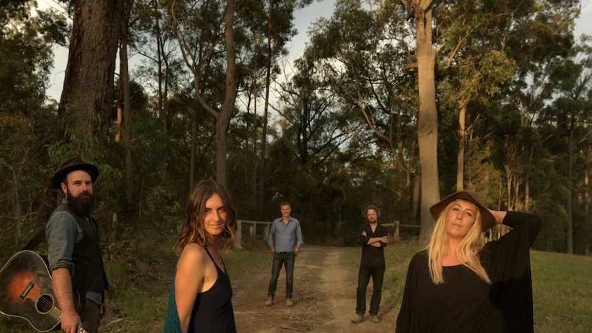 The five piece WA band The Waifs, with Vikki Thorn at front left stand on a dirt road surrounded by tall trees