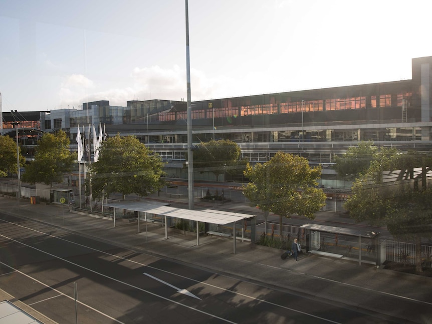 A lone traveller walks along an empty pick-up bay rank with her suitcase