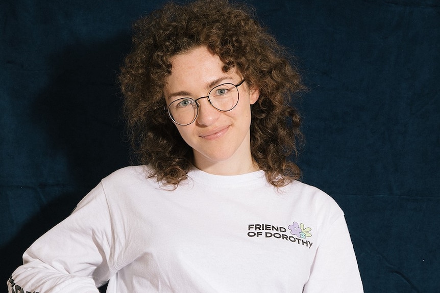 Hannah, who wears glasses and has very curly brown hair, smiles in a jumper that reads 'friend of dorothy'.