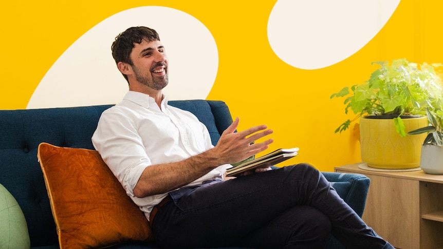 Psychologist Chris Cheers sitting on a couch, smiling mid-conversation. 