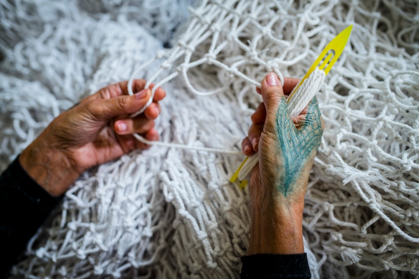 Close up photo of two hands working on weaving a white net.