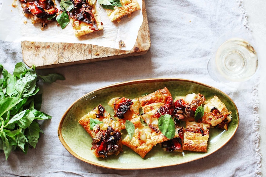 Onion, anchovy and capsicum tart sliced and served on a plate with bubbly for a summer time starter recipe.