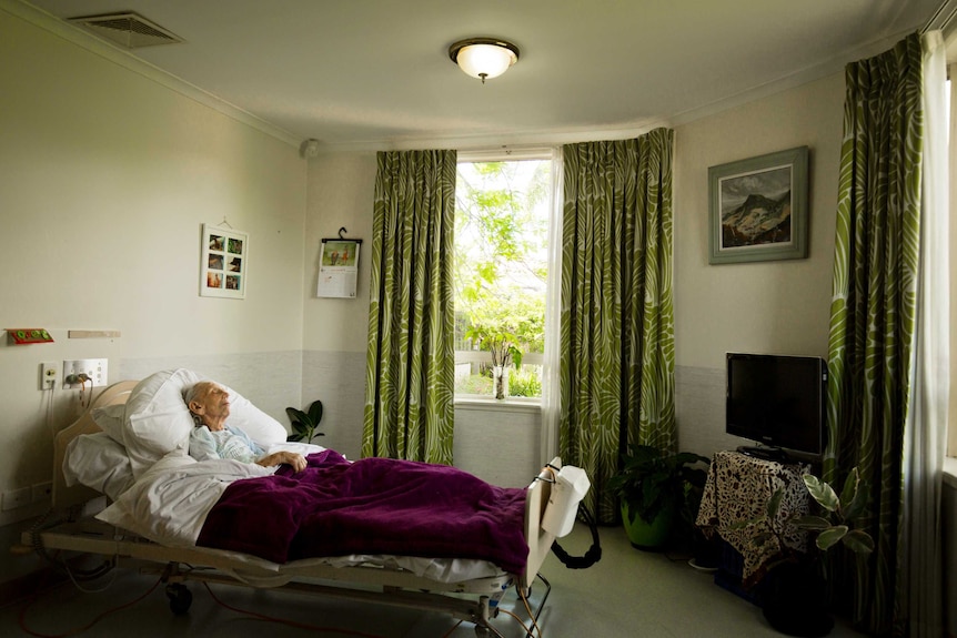 Margaret Kerans lays in bed on her own in a nursing home room.