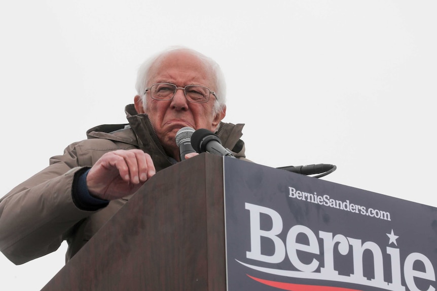 Bernie Sanders at a lectern holding a microphone