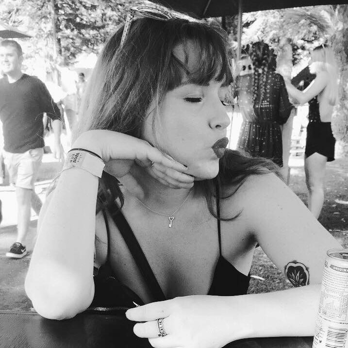 A black and white photo showing Olivia Mead sitting at a table outdoors feigning a kiss with her eyes closed.