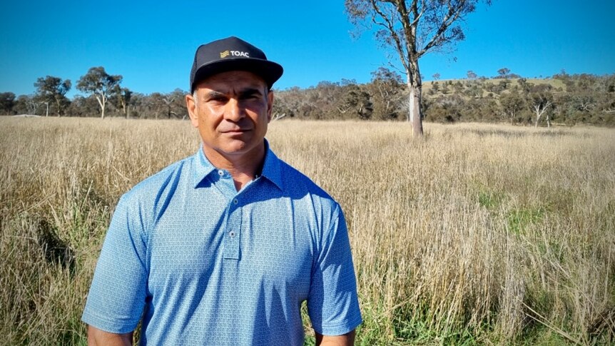 An Indigenous man stands in Canberra with a hat and blue shirt. 