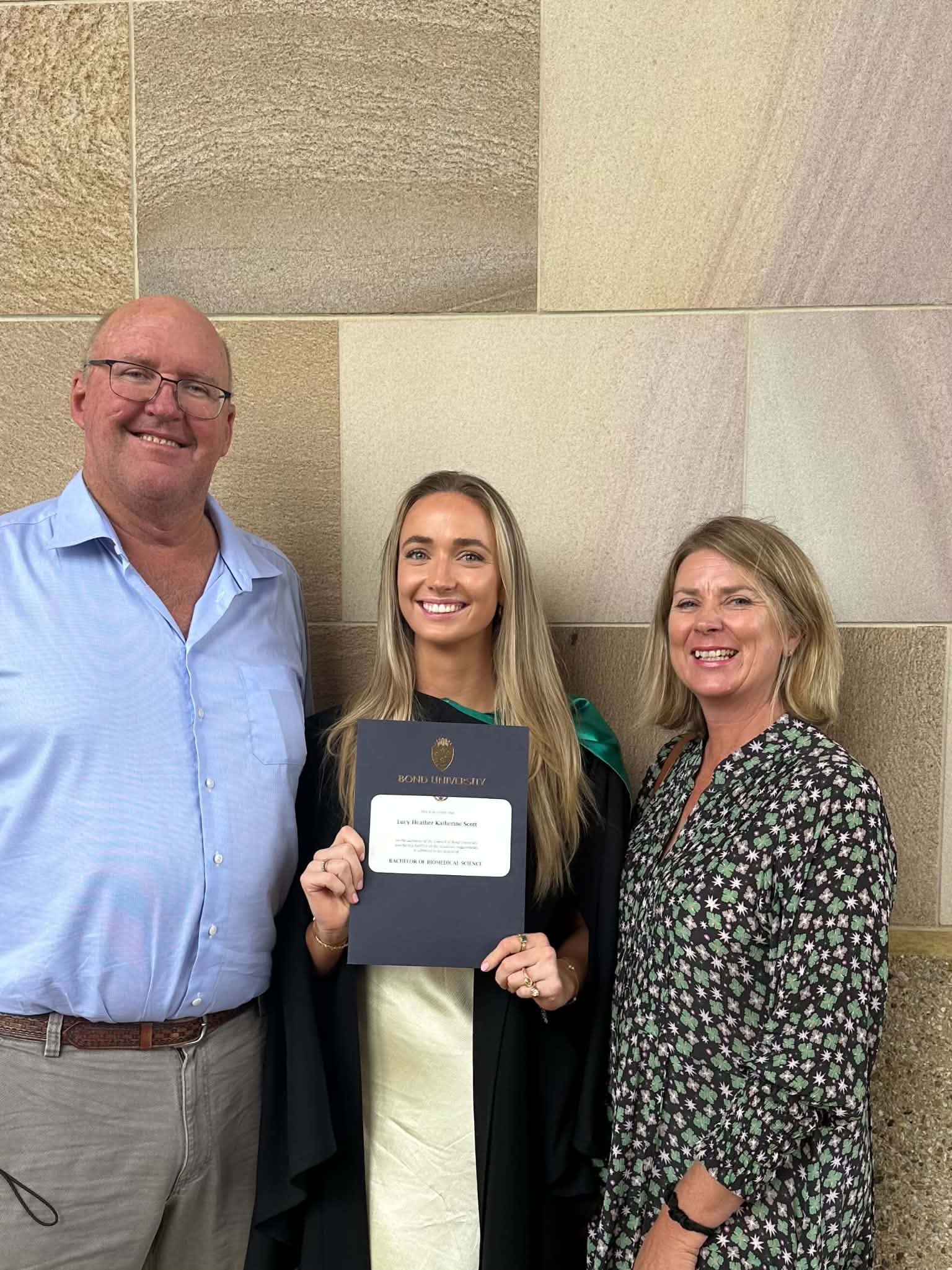 Lucy Scott holding her biomedical sciences diploma, standing with her parents on graduation day.