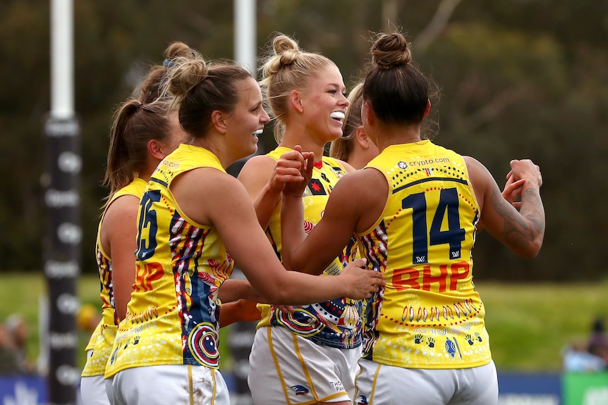 Crows players gather around Ashleigh Woodward to celebrate a goal with her