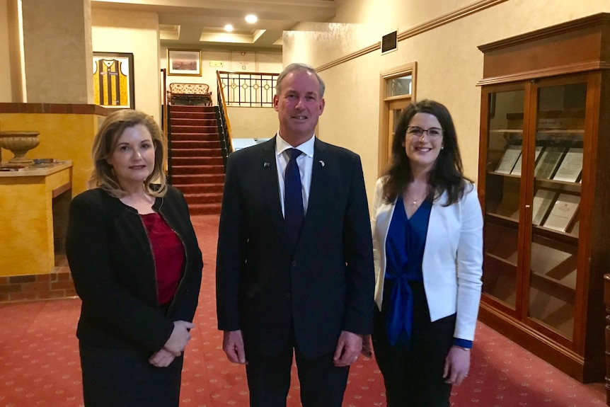 A man and two women, all dressed in suits, pose for the camera.