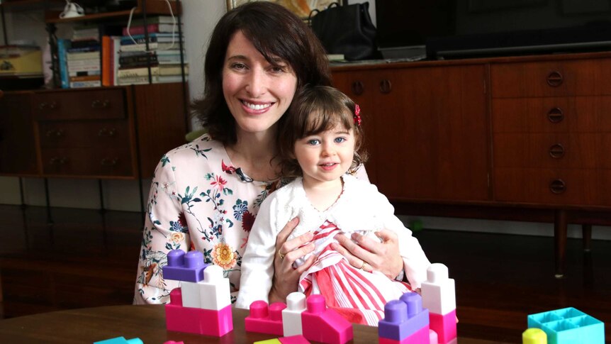 Jemma holds Amelie at a dining table with coloured blocks in the foreground.