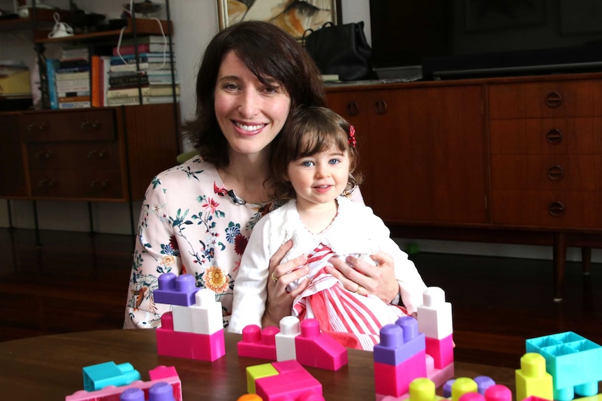 Jemma holds Amelie at a dining table with coloured blocks in the foreground.