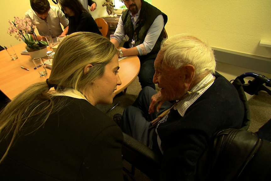 Charlotte Hamlyn leans down to come face to face with David Goodall in his wheelchair, the pair share small smiles.