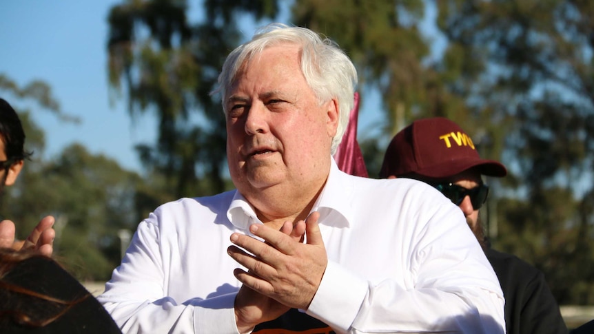 Clive Palmer claps his hands and wears a white collared shirt at a rally in Canberra.