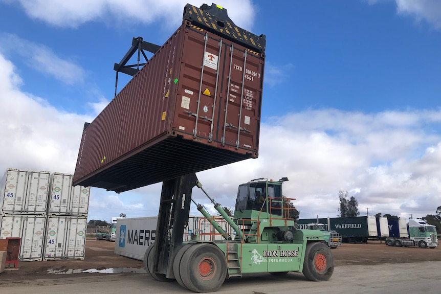 A large machine is being used to carry a brown shipping container