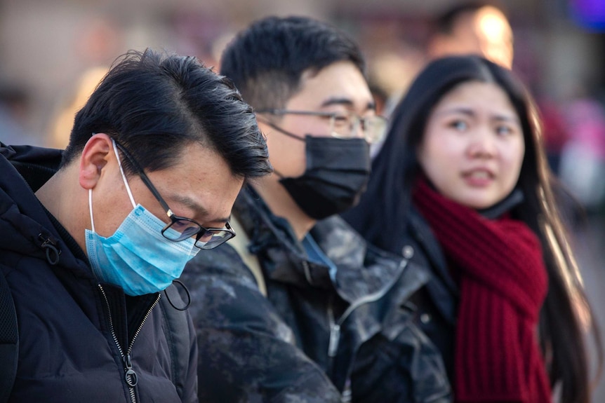 Travelers wear face masks as they walk outside of the Beijing Railway Station.