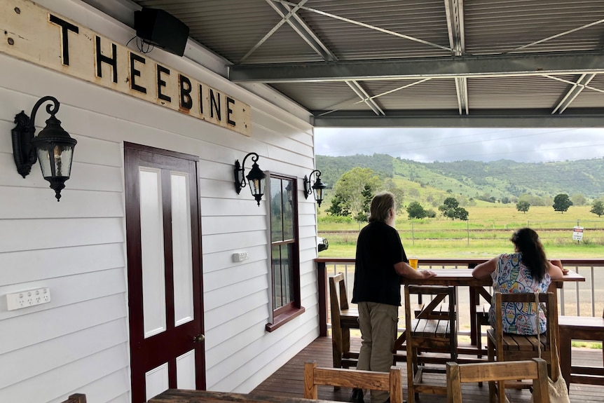 Two people sit at tables looking out towards a mountain.