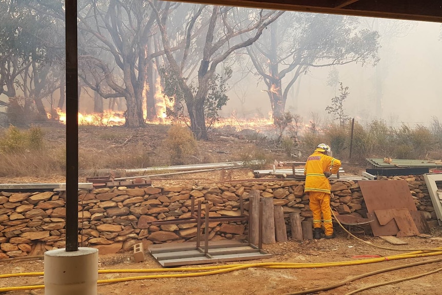 A fire comes close to a rock wall at the back of a rural property.