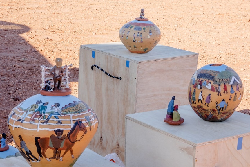 Three colourfully painted ceramic pots on timber boxes in the desert.