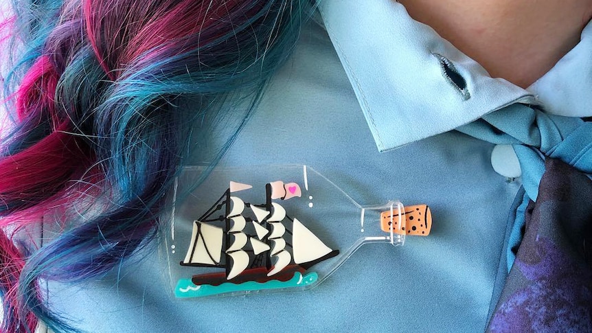 Woman with pink and blue hair wears ship in a bottle brooch to depict how to wear brooches for personal style.